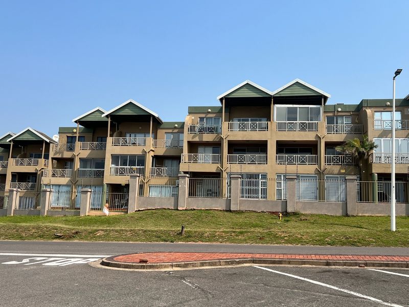 A multi-story apartment complex featuring gabled rooflines, private balconies, and secure perimeter fencing, viewed from the street level.