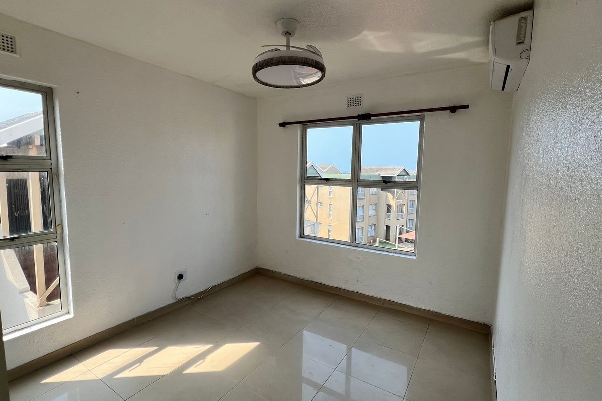A bright, empty bedroom featuring tiled flooring, an air conditioning unit, and large windows providing natural light and an urban view.