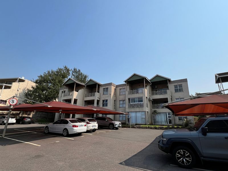 Exterior view of the apartment complex featuring a paved parking area with shade cloth carports and residential balconies.