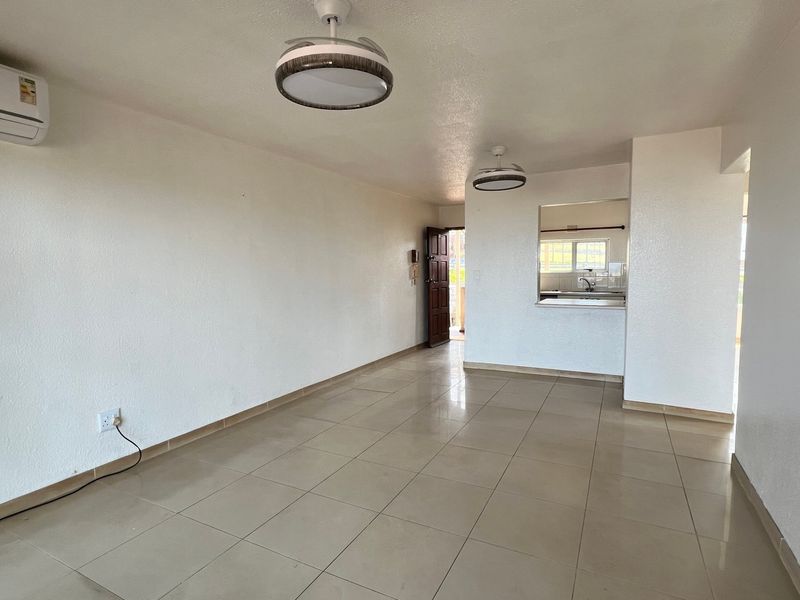 Spacious open-plan living area featuring neutral tiled flooring, a split-system air conditioner, and a convenient kitchen pass-through window.