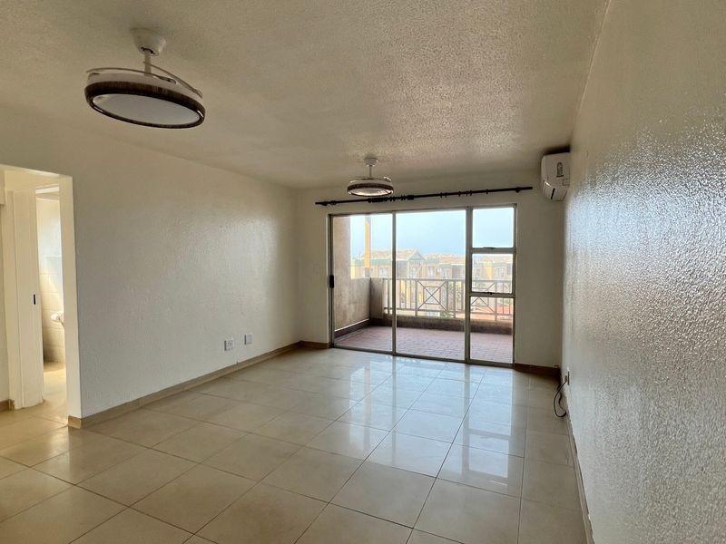 Spacious, empty living area featuring neutral tiled flooring, modern ceiling lights, wall-mounted air conditioning, and direct access to a private balcony.