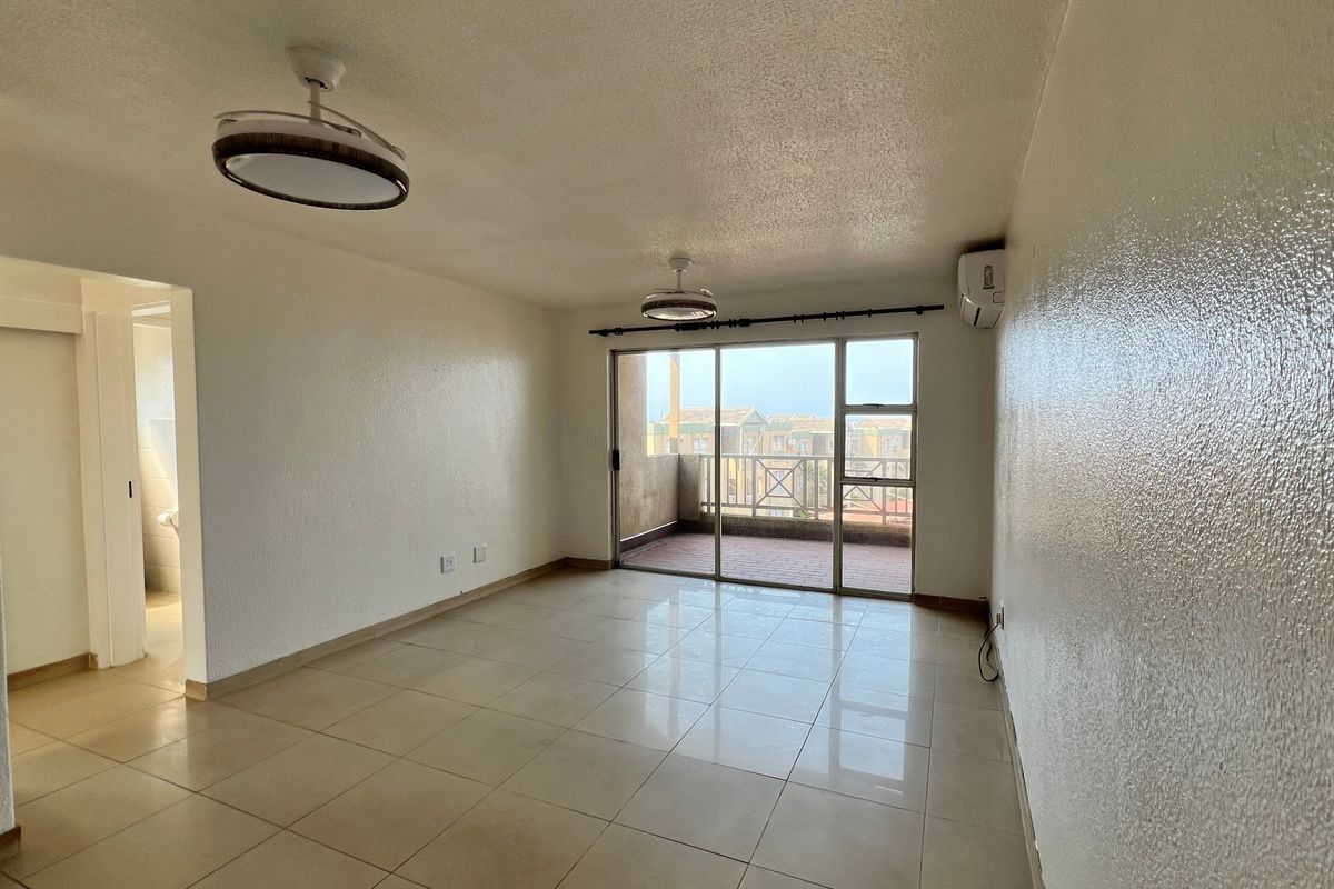 Spacious, empty living area featuring neutral tiled flooring, modern ceiling lights, wall-mounted air conditioning, and direct access to a private balcony.