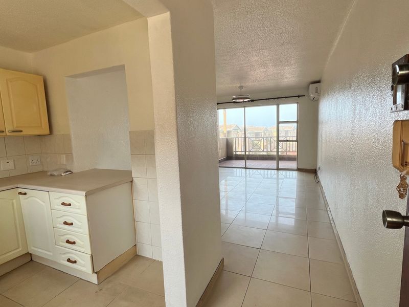 Open-plan kitchen and living area featuring tiled floors, neutral walls, and a sliding glass door leading to a private balcony.