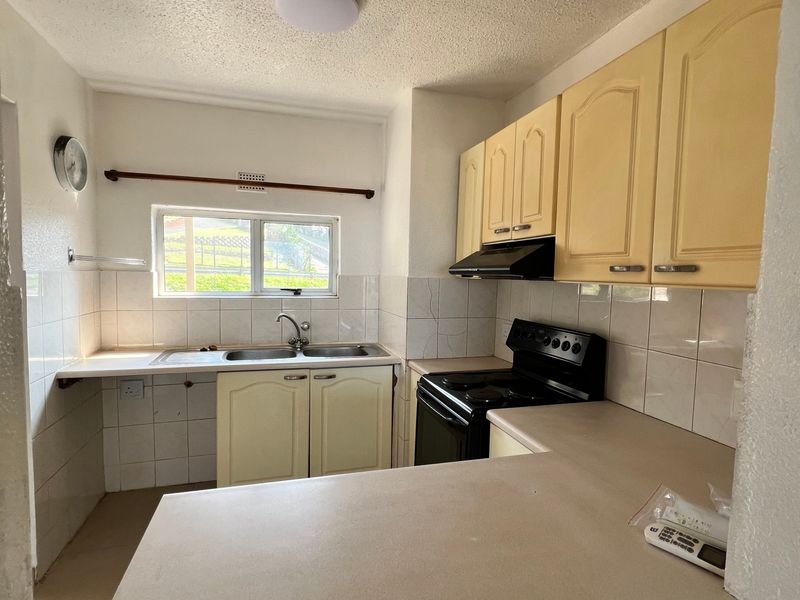 A functional kitchen featuring built-in cabinetry, a double basin sink, tiled backsplash, and an electric stove, offering potential for modern updates.