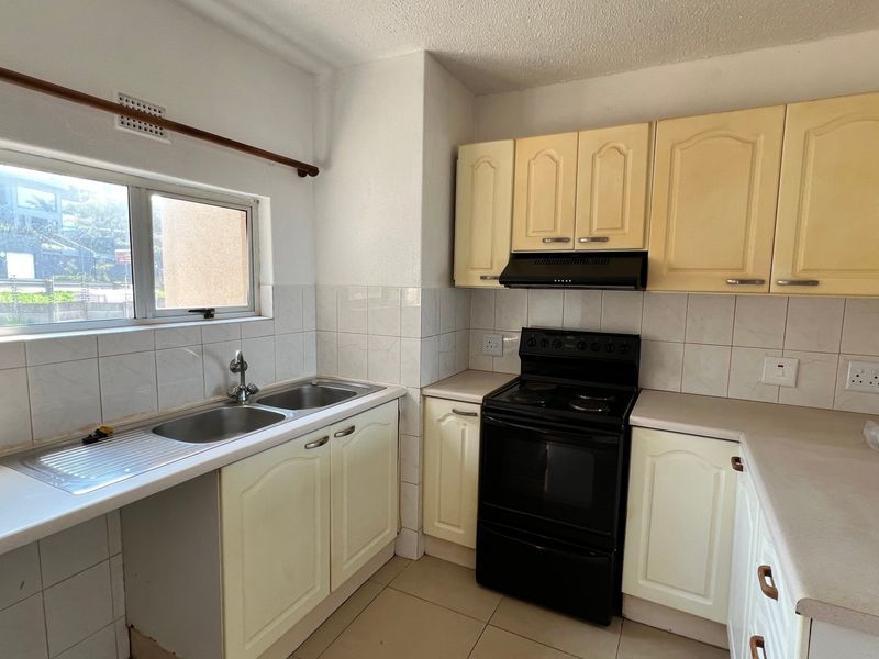 A functional kitchen featuring built-in cabinetry, a double basin sink, tiled backsplash, and a freestanding electric stove with an extractor fan.