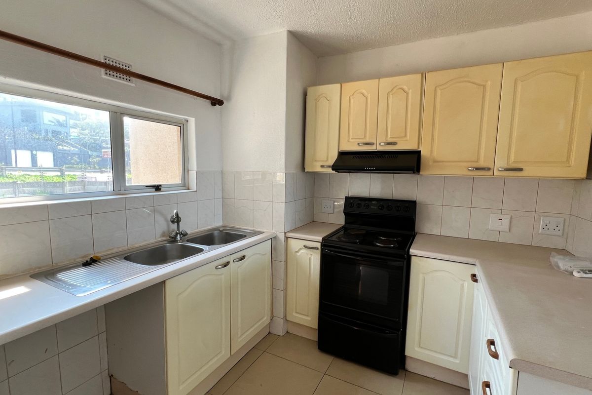 A functional kitchen featuring built-in cabinetry, a double basin sink, tiled backsplash, and a freestanding electric stove with an extractor fan.