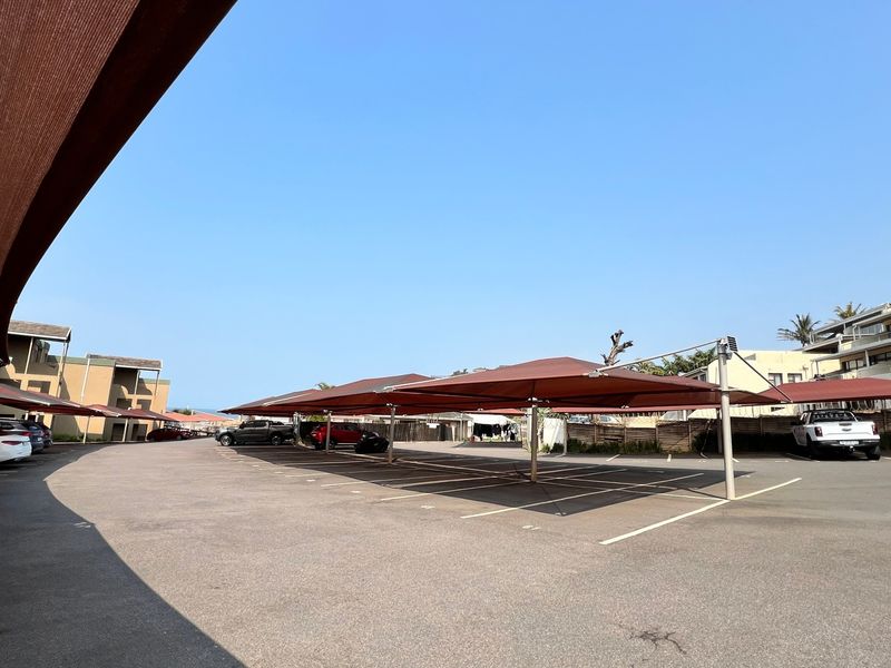 A well-maintained outdoor parking area featuring multiple shade cloth carports and clearly marked asphalt parking bays for residents.