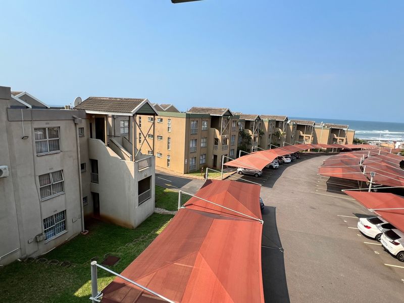 Aerial view of the apartment complex featuring covered parking bays, paved driveways, and exterior building facades with ocean views in the distance.
