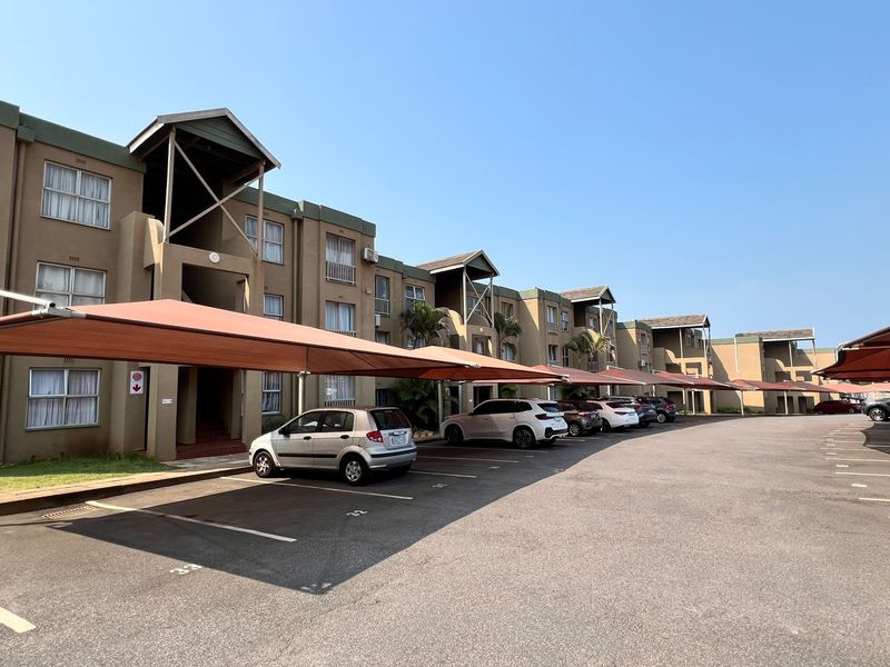 Exterior view of a multi-story apartment complex featuring covered parking bays and paved driveway access.