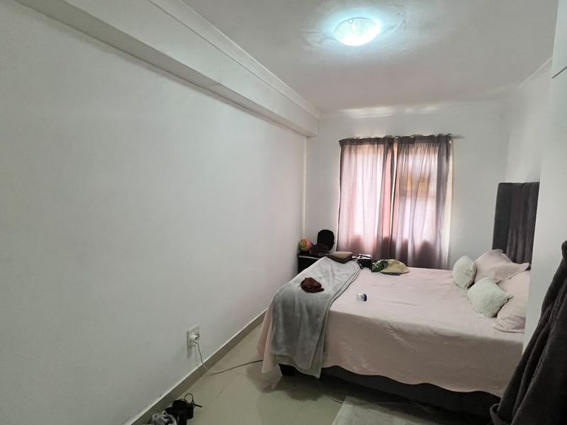 A standard bedroom featuring tiled flooring, neutral walls, and a ceiling light fixture, offering a functional space with natural light from the window.