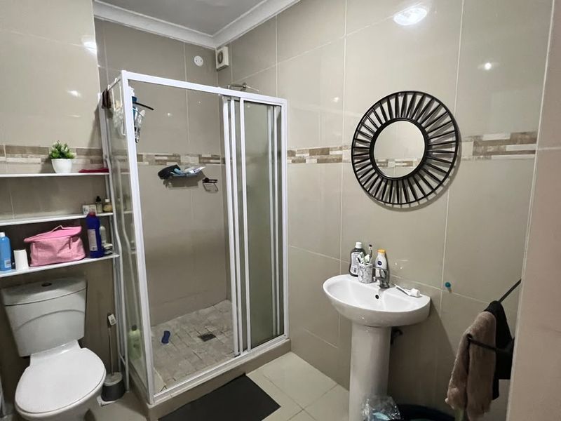 A functional bathroom featuring a shower enclosure, pedestal basin, and toilet with neutral wall and floor tiling.
