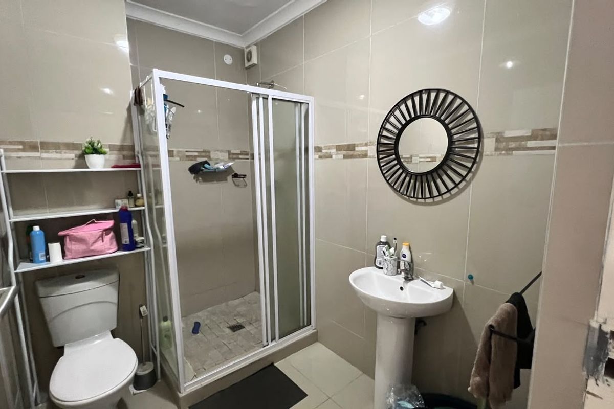 A functional bathroom featuring a shower enclosure, pedestal basin, and toilet with neutral wall and floor tiling.