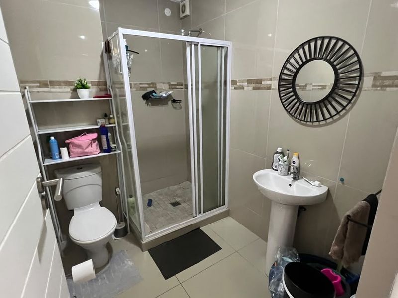 A functional bathroom featuring a shower enclosure, pedestal basin, and toilet with neutral wall and floor tiling.