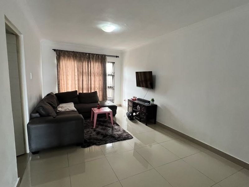 A functional living room featuring neutral tiled flooring and a wall-mounted television setup, offering a clean and versatile space for relaxation.