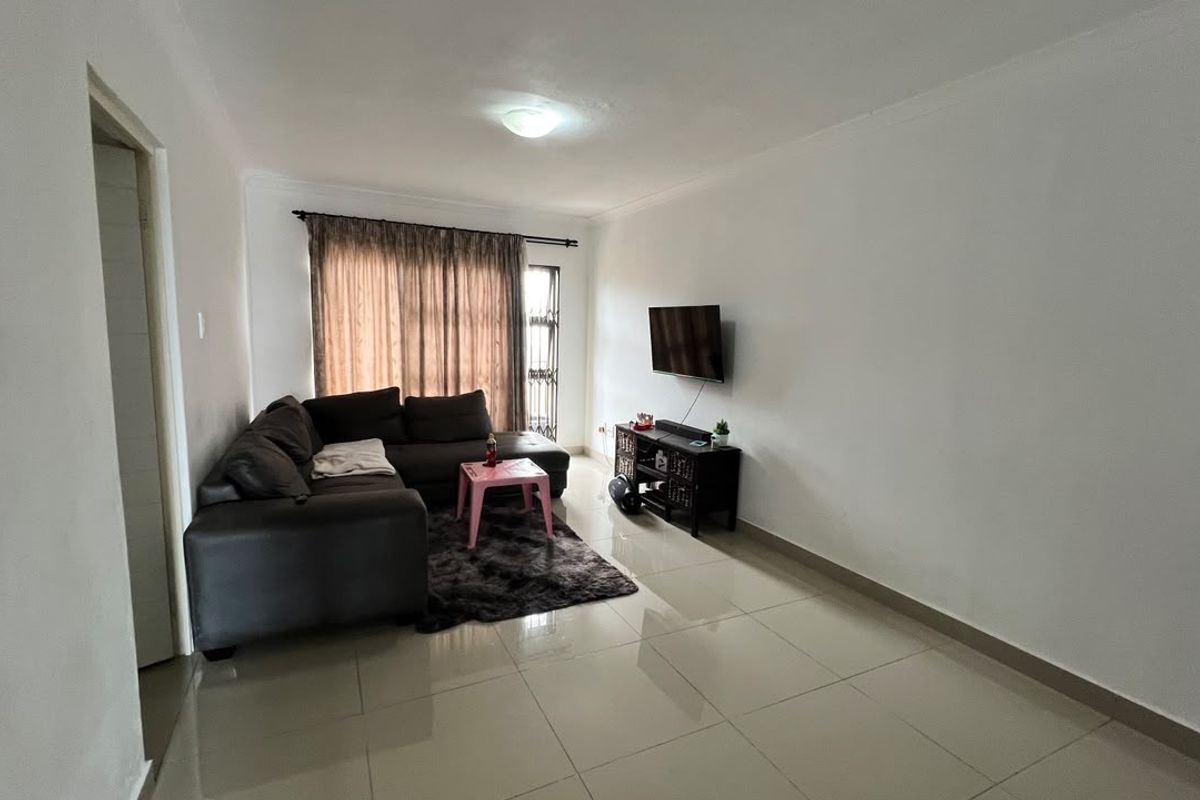 A functional living room featuring neutral tiled flooring and a wall-mounted television setup, offering a clean and versatile space for relaxation.