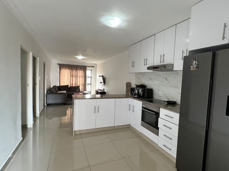 Open-plan living area featuring a modern kitchen with white cabinetry, stone countertops, and integrated appliances, flowing into a spacious lounge area.