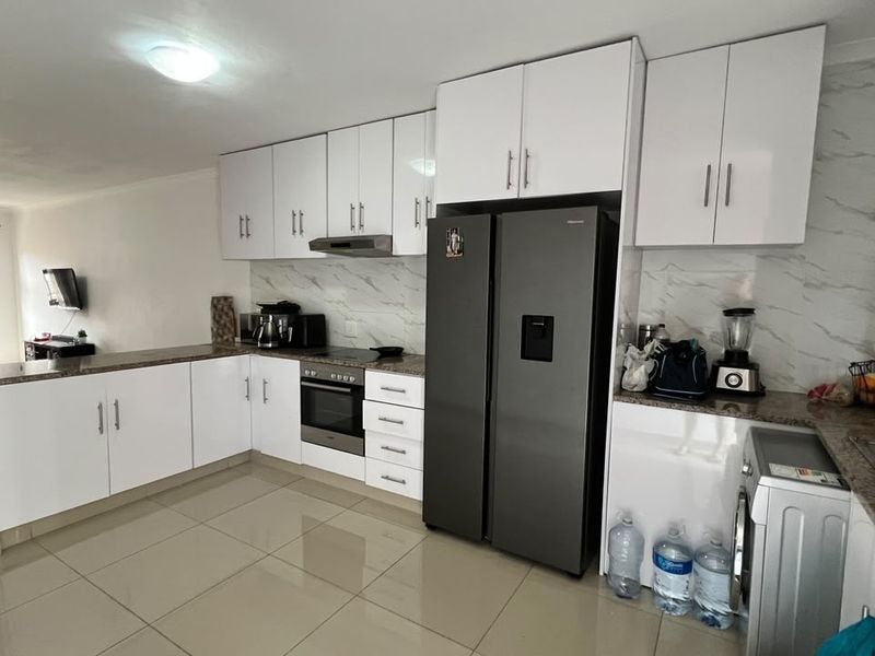 Modern open-plan kitchen featuring white gloss cabinetry, granite countertops, marble-effect splashback, and integrated appliances, seamlessly flowing into the adjacent living area.