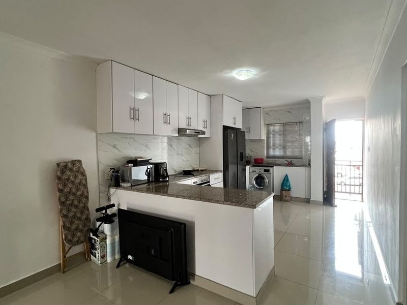 Open plan kitchen featuring granite countertops, white cabinetry, and integrated appliances, leading to a bright living area with direct access to a balcony.
