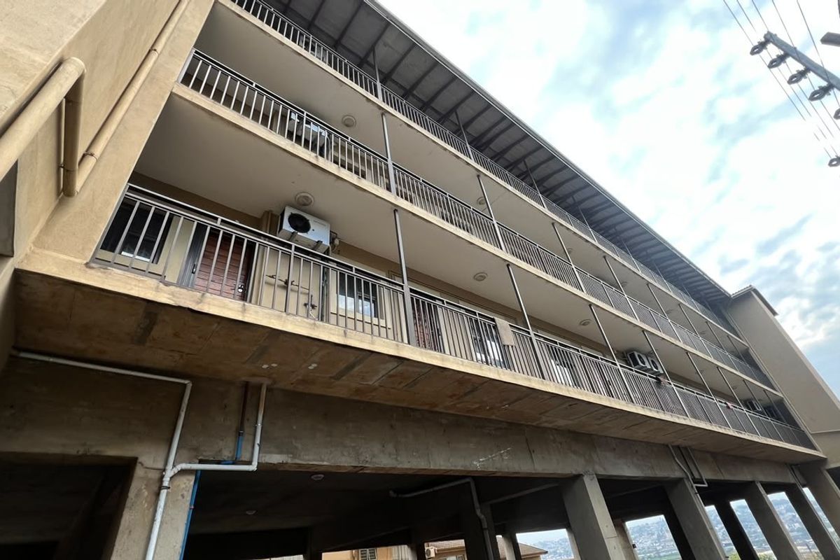 Exterior view of an apartment building featuring multiple levels of balconies with metal railings and visible air conditioning units.