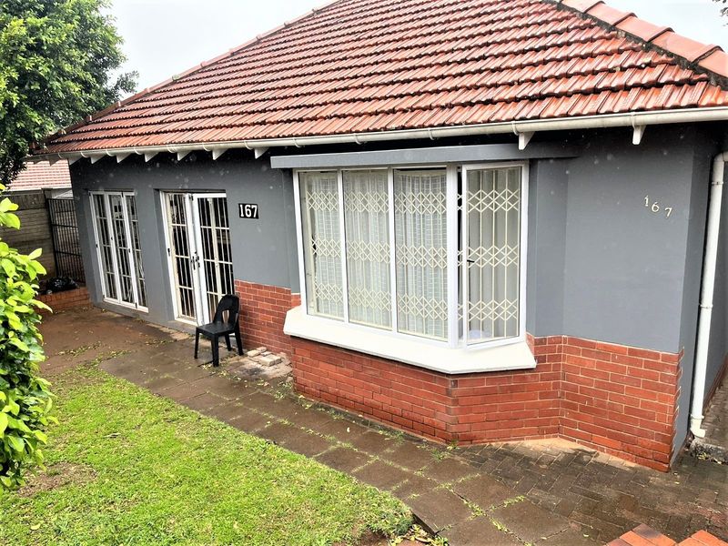 Front elevation of a single-story house featuring a terracotta tiled roof, bay window with security gates, and a combination of brick and painted wall finishes.