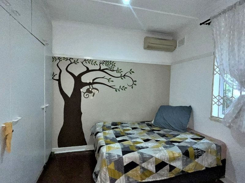 A bedroom featuring built-in cupboards, an air conditioning unit, and security bars on the window.