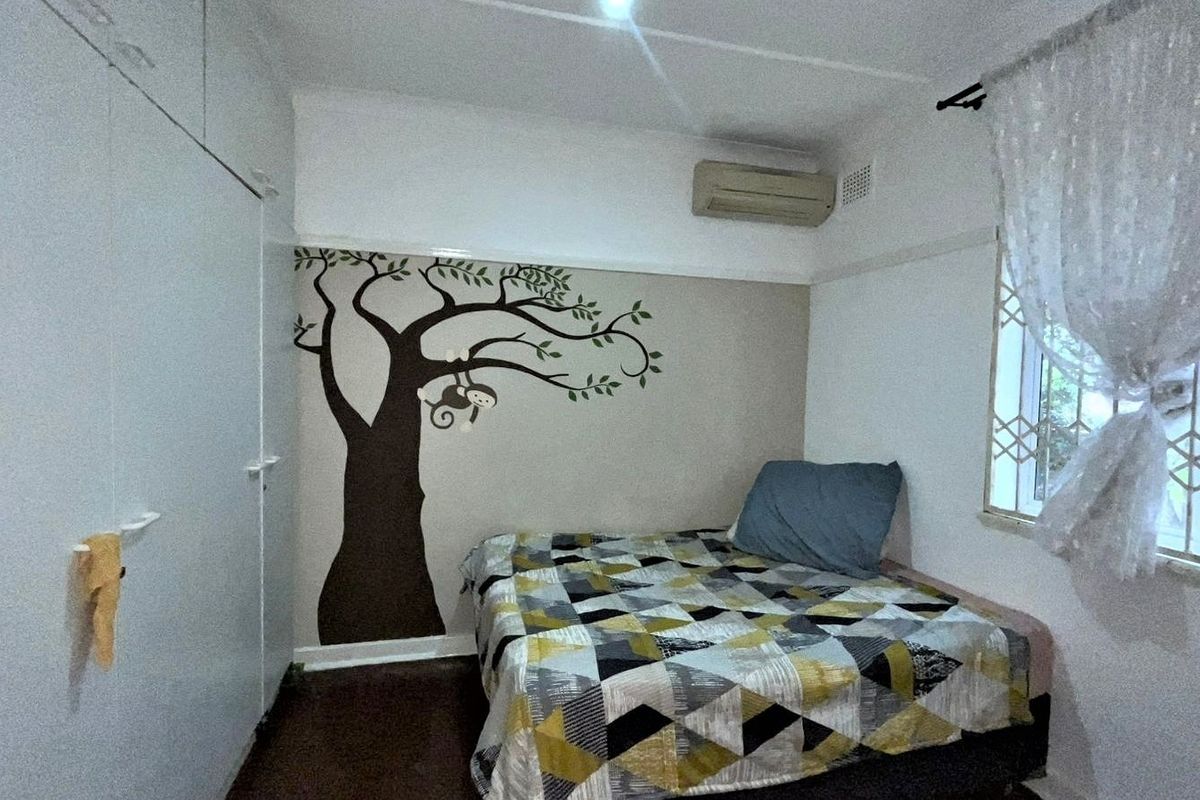 A bedroom featuring built-in cupboards, an air conditioning unit, and security bars on the window.
