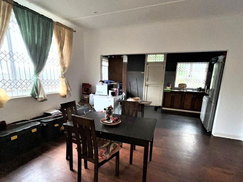 Open-plan living and kitchen area featuring dark flooring, window security bars, and dated kitchen cabinetry.