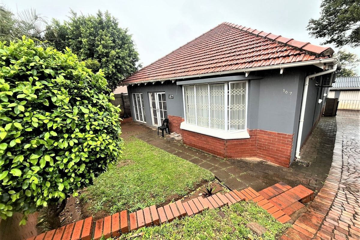 Front elevation of a single-story house featuring a tiled roof, brick and painted facade, bay window, and paved driveway access.