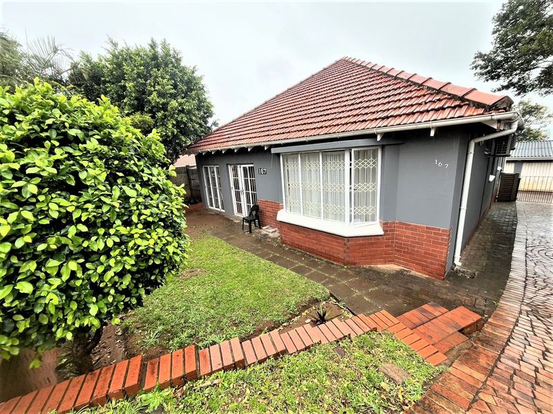 Front elevation of a single-story house featuring a tiled roof, brick and painted facade, bay window, and paved driveway access.