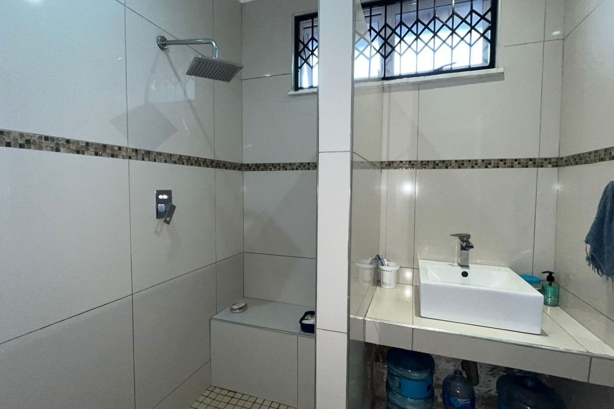 A functional bathroom featuring a tiled walk-in shower with a built-in bench, a vessel sink on a tiled vanity, and security bars on the window.