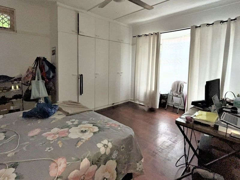 Spacious bedroom featuring built-in cupboards, timber flooring, and a ceiling fan, with natural light provided by large windows.