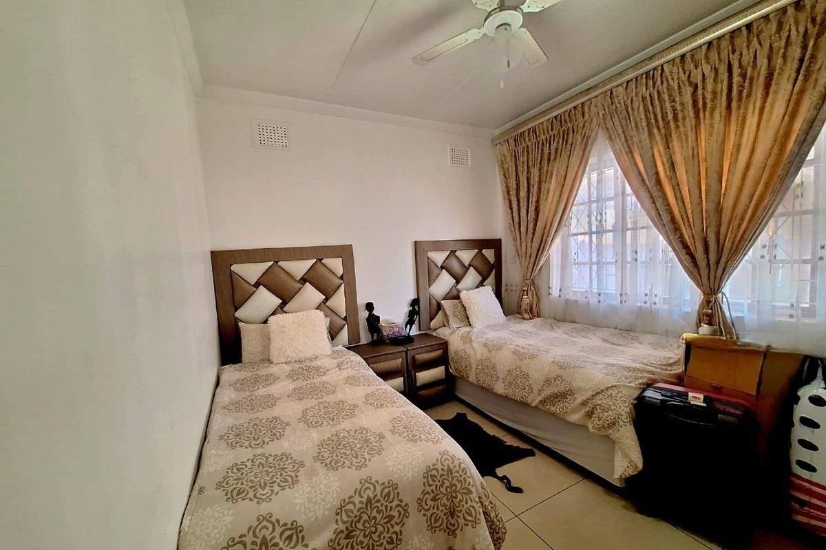 A bedroom featuring tiled flooring, a ceiling fan, and window security bars, providing a functional space with natural light.