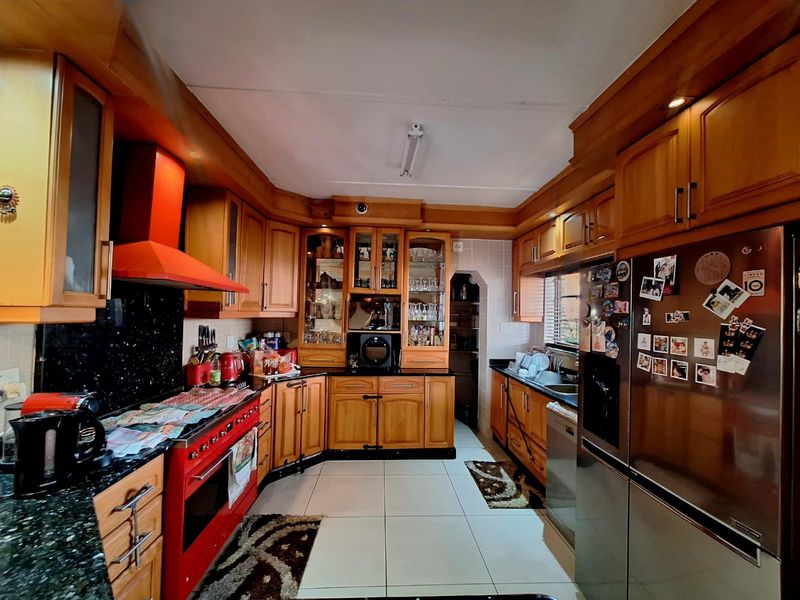 A traditional kitchen featuring extensive wooden cabinetry, granite countertops, a distinctive red range cooker, and tiled flooring.