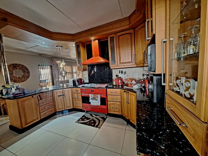 A spacious kitchen featuring wooden cabinetry, granite countertops, and a prominent red freestanding oven with a matching extractor fan.