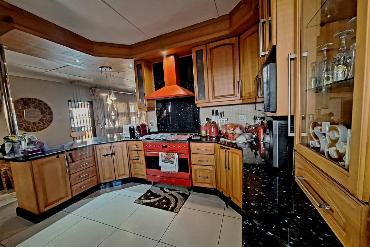 A spacious kitchen featuring wooden cabinetry, granite countertops, and a prominent red freestanding oven with a matching extractor fan.