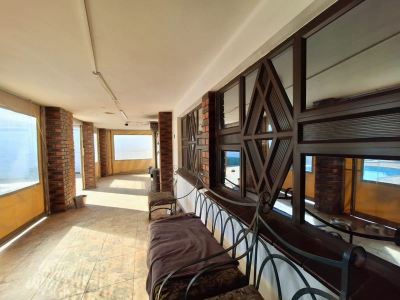 A covered patio area featuring brick pillars, tiled flooring, and decorative timber window frames, enclosed with retractable weather blinds.
