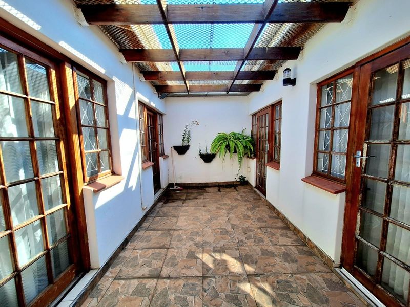 A covered patio area featuring a timber pergola, tiled flooring, and multiple timber-framed glass doors providing access to the surrounding living spaces.