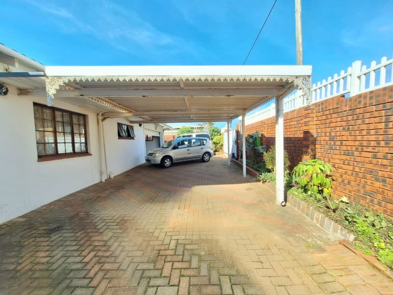 A covered carport area featuring brick paving and a brick boundary wall, providing sheltered off-street parking.