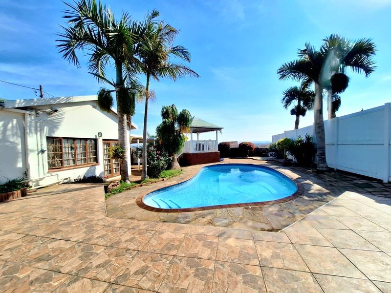A well-maintained outdoor pool area featuring a paved patio, a charming gazebo, and established palm trees, perfect for relaxation and outdoor entertaining.