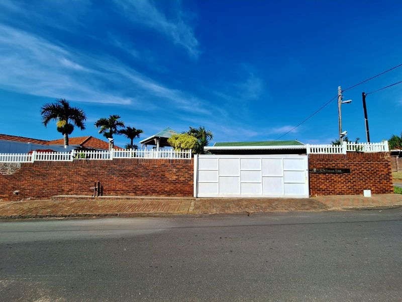 Street-facing view of the property featuring a solid white driveway gate, brick boundary wall with white picket fencing, and paved sidewalk.
