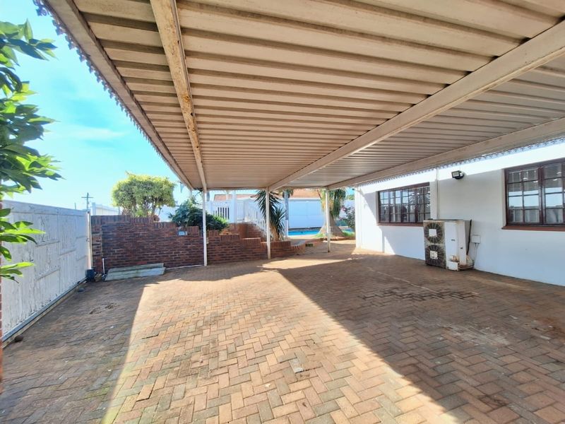 Covered outdoor patio area featuring brick paving, a corrugated metal roof structure, and a brick retaining wall, providing a functional space for outdoor living.