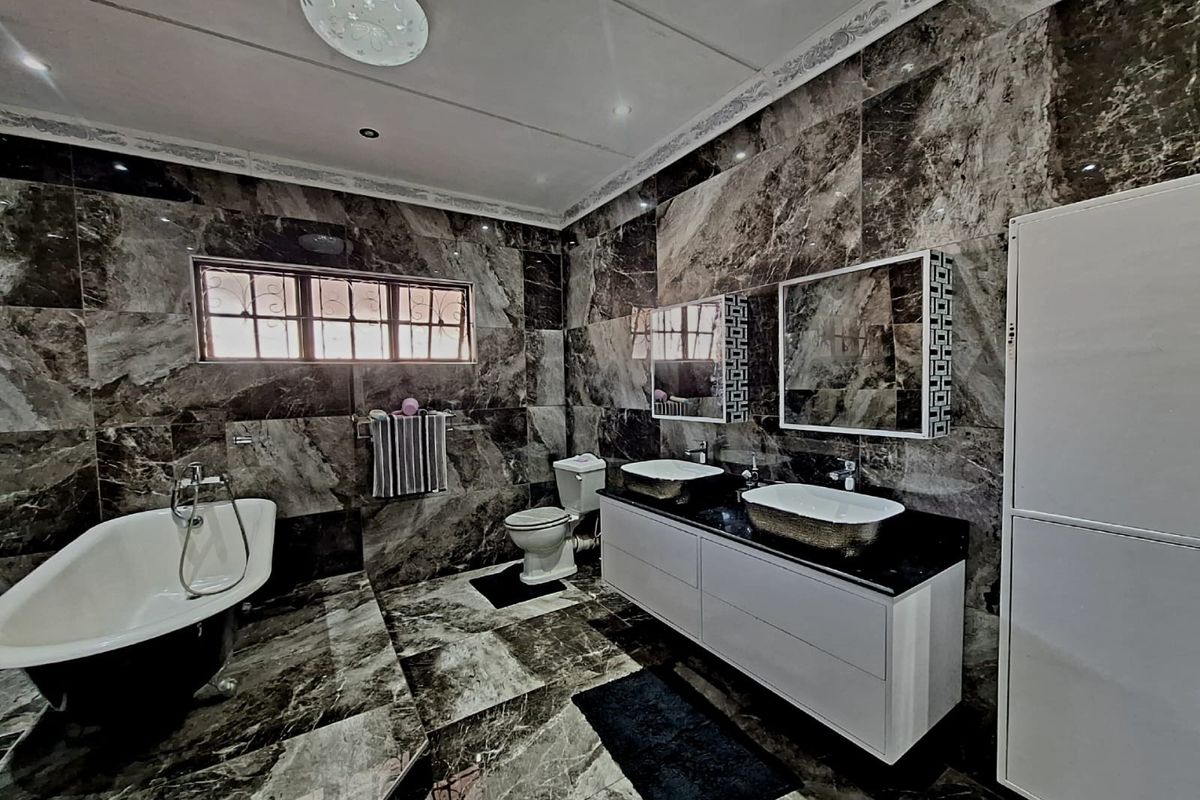 Modern bathroom featuring a freestanding bathtub, double vanity with vessel sinks, and full-height marble wall and floor tiling.