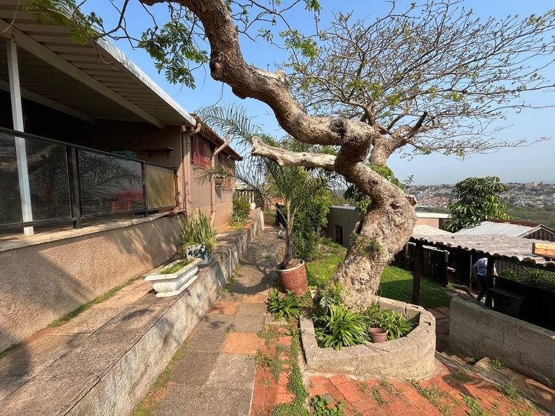 Rear exterior area featuring a paved walkway, raised planter beds, and a covered patio space with a glass balustrade overlooking the surrounding neighborhood.