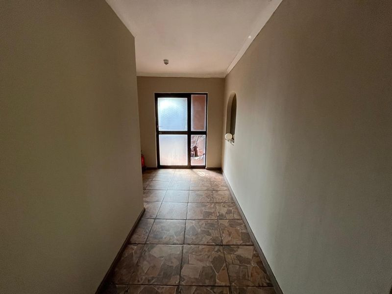 A vacant hallway featuring tiled flooring and an archway, leading to an exterior door with a damaged glass panel.