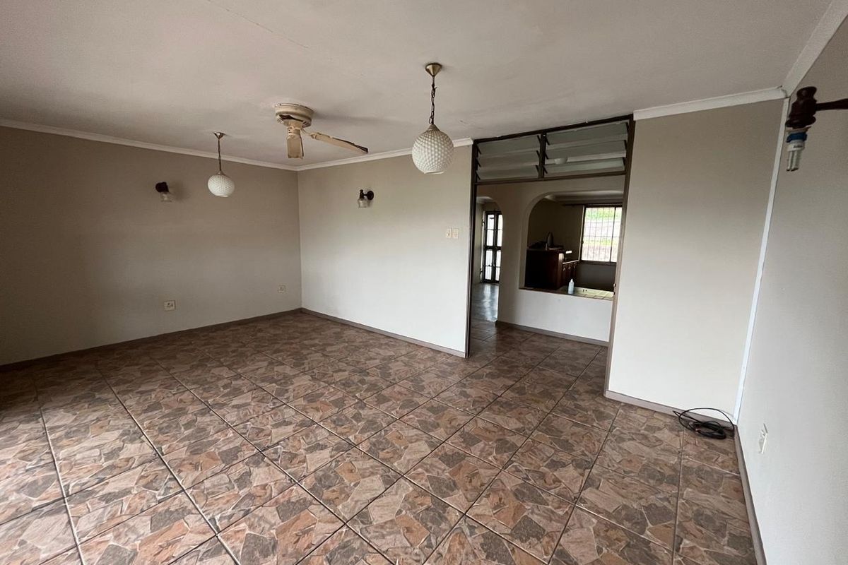 An empty living room featuring tiled flooring, ceiling fan, and wall lighting, with an open archway leading to an adjacent space.