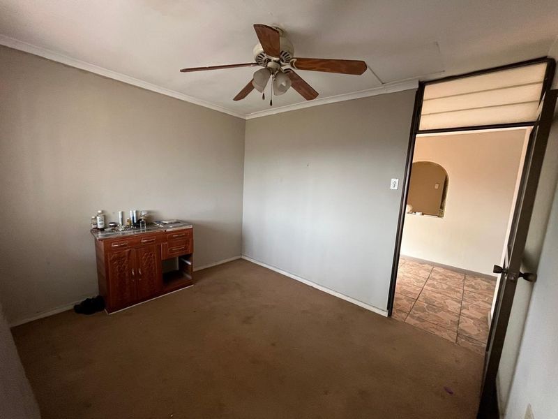 A vacant bedroom featuring a ceiling fan and carpeted flooring, requiring cosmetic updates to improve its overall condition and appeal.