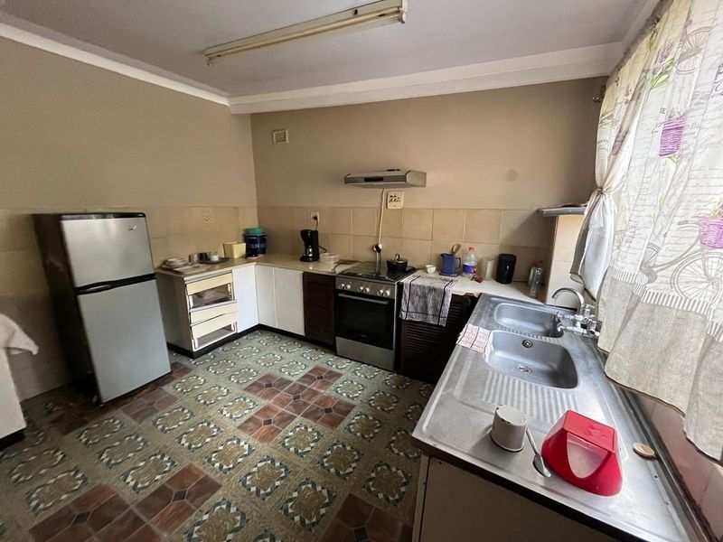 A functional kitchen featuring built-in cabinetry, a stainless steel double sink, a freestanding stove with extractor fan, and patterned floor tiles.