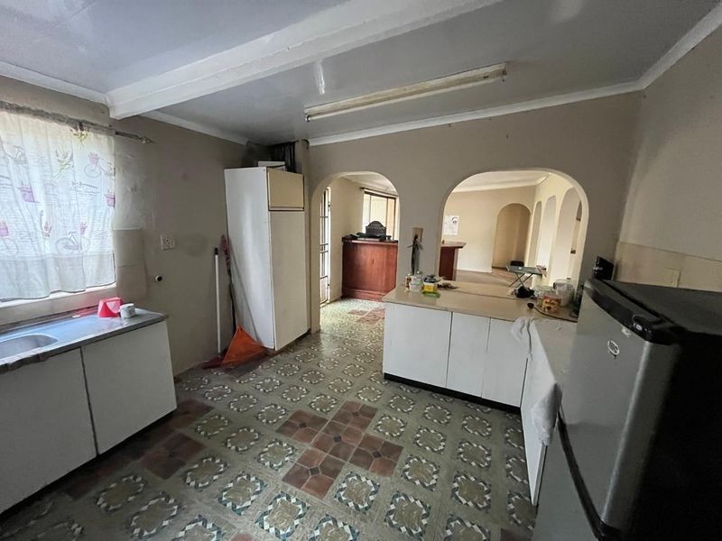 A dated kitchen featuring original patterned floor tiles, built-in cabinetry, and arched doorways leading to adjacent living spaces.