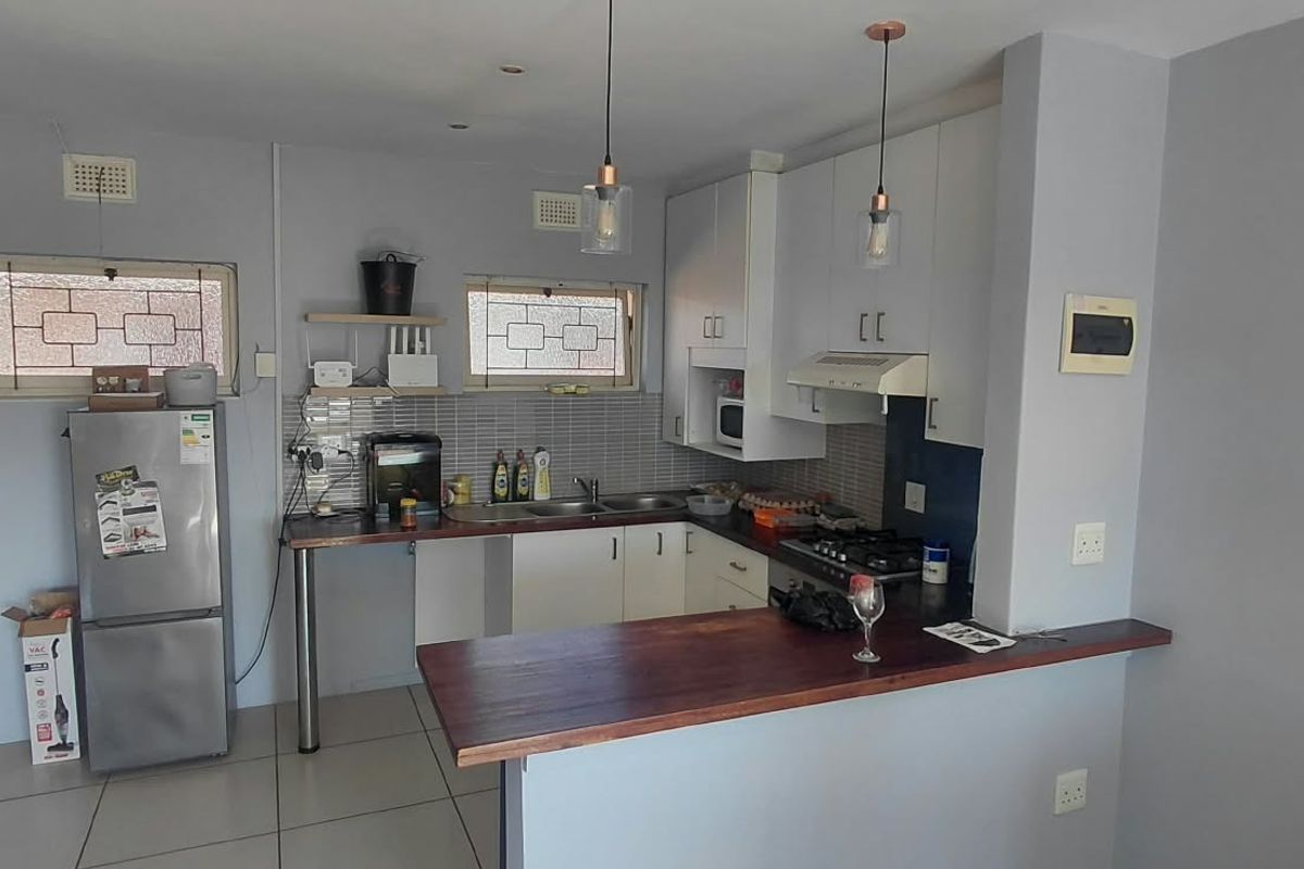 Functional kitchen featuring white cabinetry, a wooden breakfast bar, gas hob, extractor fan, and tiled backsplash with ample counter space.