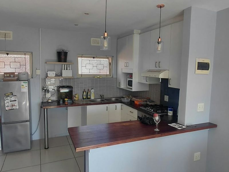 Functional kitchen featuring white cabinetry, a wooden breakfast bar, gas hob, extractor fan, and tiled backsplash with ample counter space.